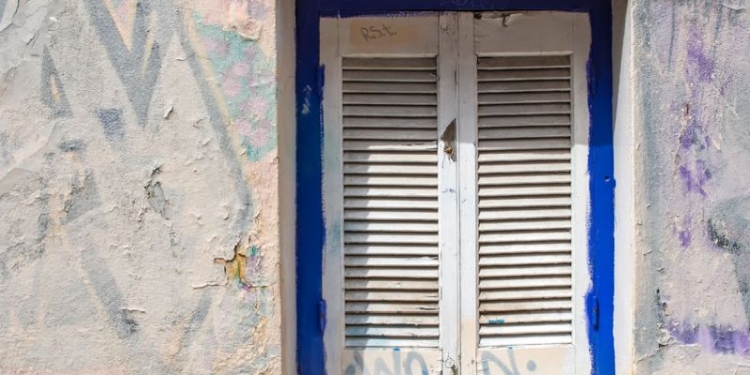 54216496 - blue framed window with white closed shutter. wall of the house with partly covered graffiti. plaka, athens, greece.