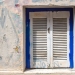 54216496 - blue framed window with white closed shutter. wall of the house with partly covered graffiti. plaka, athens, greece.