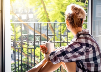 52650465 - young pretty woman  sitting at opened window drinking coffee and looking outside enjoys of rest